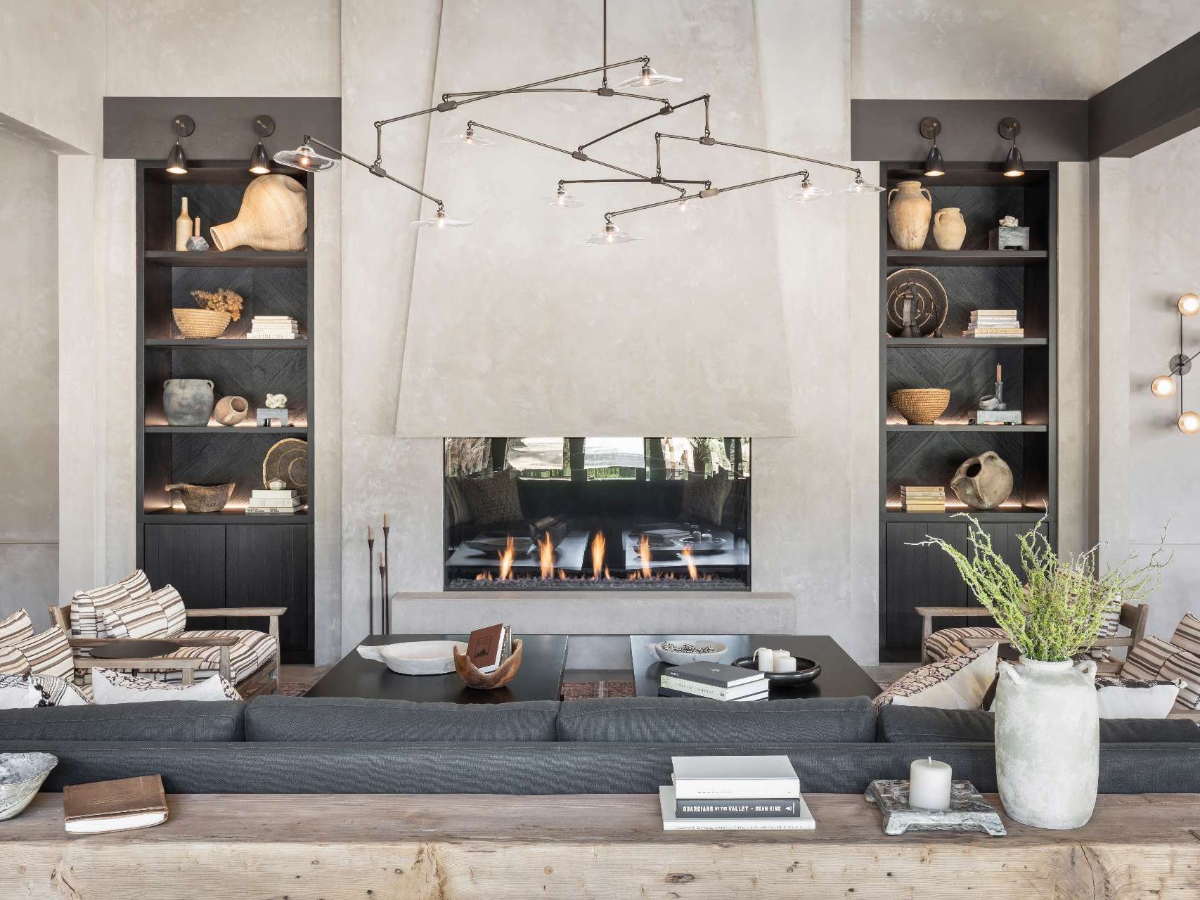 Inside this wine tasting room, the palette leans natural and textural. Plastered walls meet polished concrete floors, and a dark-stained wood ceiling adds warmth overhead. Cabinets made from Shou Sugi ban (charred wood) bring depth without shouting for attention. A central fireplace marks the heart of the space, surrounded by relaxed lounge seating.  Nothing feels overdesigned, yet everything has presence.